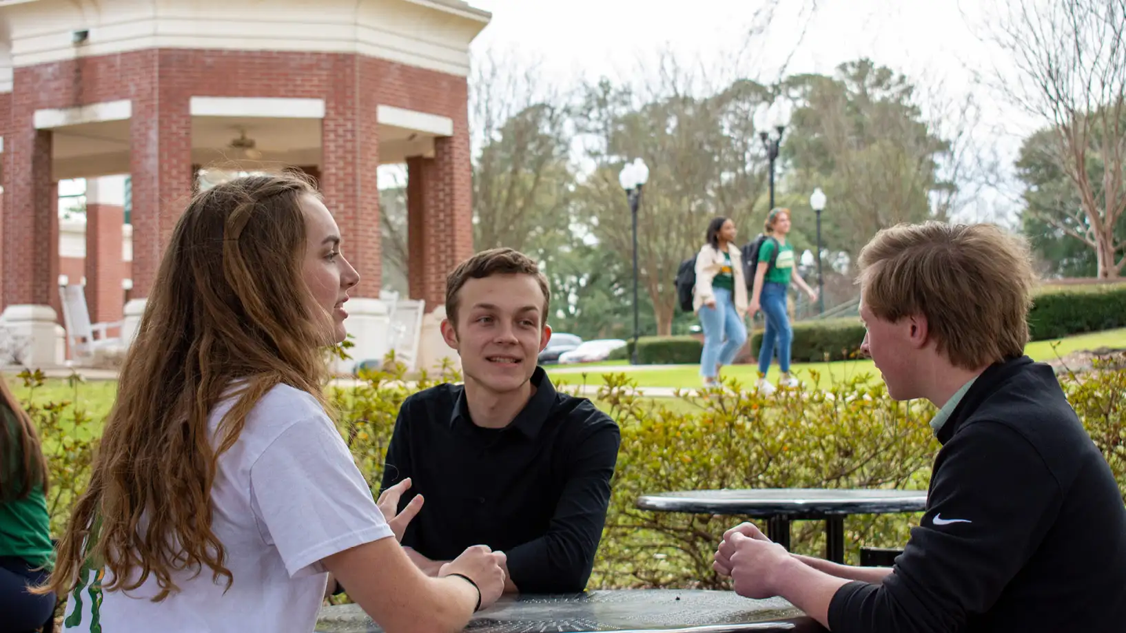 three students chatting at an outdoor table