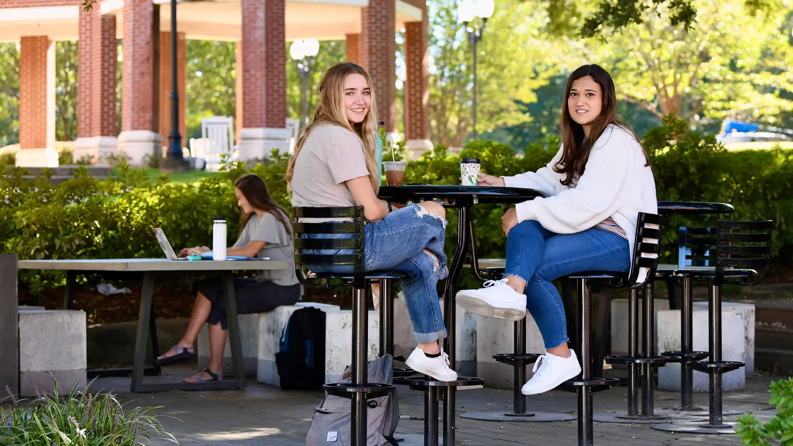 two girls in jeans visiting over coffee outside