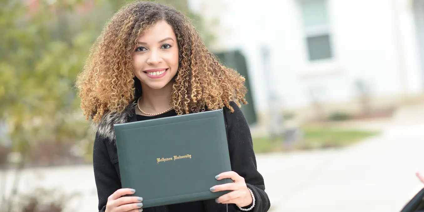 Belhaven student with diploma by fountain, smiling