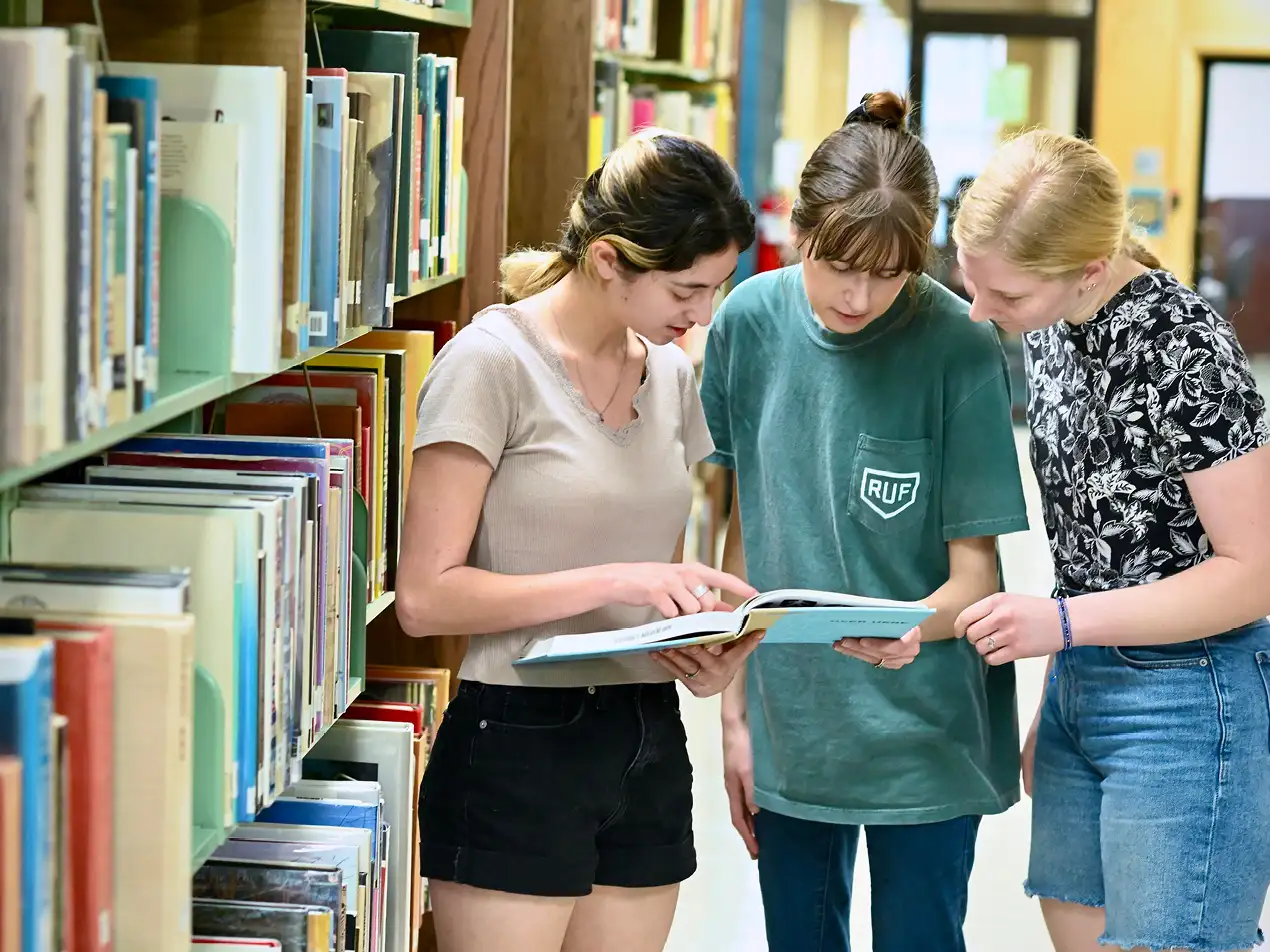 three students reading from the same book