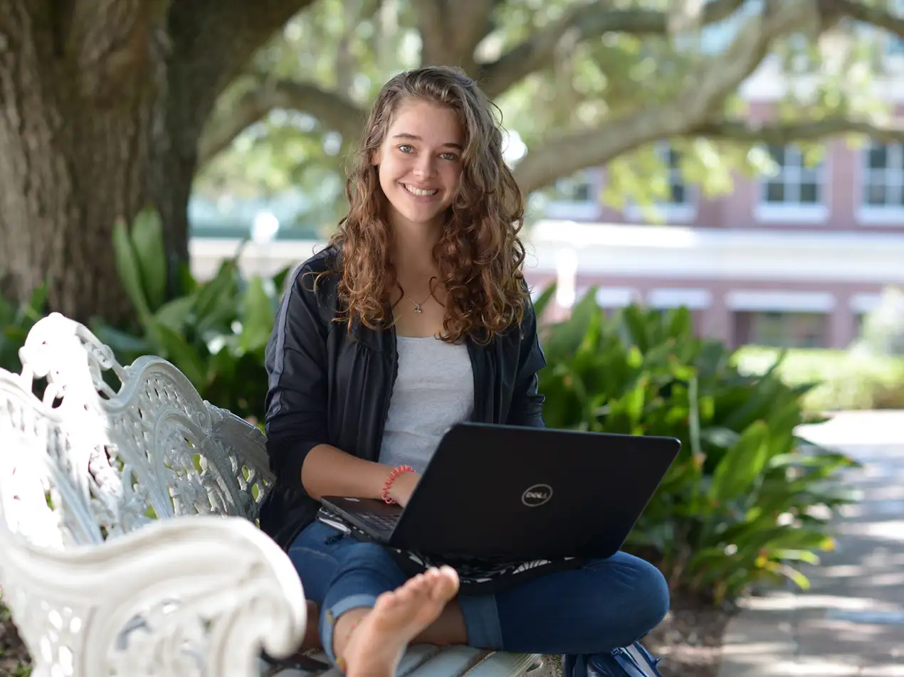 a student smiling on a bench with a laptop