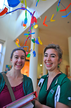 Two students smiling under a piece of student-made art